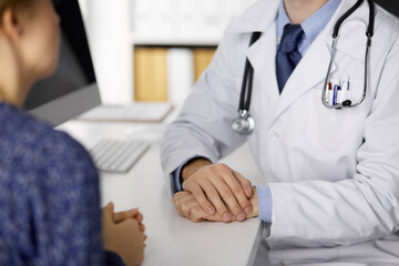 Unknown male doctor and patient woman discussing current health examination while sitting and using...