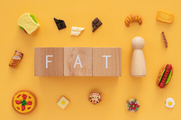 肥満、太い｜「FAT」と書かれた積み木と人型オブジェと食べ物のおもちゃ
