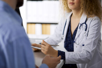 Female doctor and male patient discussing current health examination while sitting in clinic,...