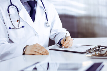 Unknown male doctor sitting and working with clipboard of medication history record in clinic at his working place, close-up. Young physician at work. Perfect medical service, medicine concept