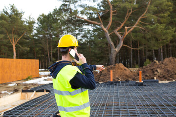 Construction worker talks on a smartphone in a yellow helmet and protective vest against the...
