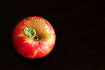 Red yellow ripe whole apple with green small leaf stands on a wooden dark brown table. Top view. Place for text