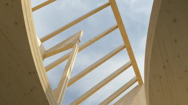 BOTTOM UP: Gentle spring sunbeams shine on the unfinished CLT house without a roof. Clear blue summer sky spans above the roof beams and the top floor of a glued-laminated timber housing project.