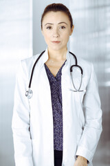 Intelligent professional woman-doctor is standing at the table in a clinic office. Portrait of friendly female physician with a stethoscope at work. Perfect medical service in a hospital. Medicine