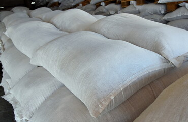 There are large gray bags of fertilizer stacked in the warehouse.