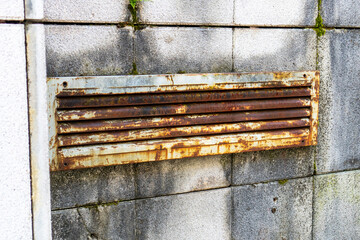 Old rusty shabby ventilation grill on a mossy tiled wall