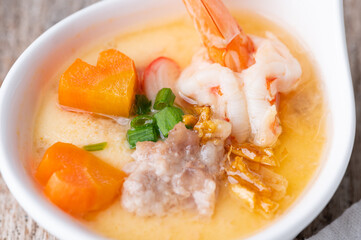 Homemade style steamed egg with shrimp and vegetables in a ceramic bowl on wooden table. healthy food concept.