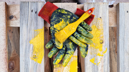 Black work protective gloves and a paintbrush smeared with yellow paint lie on a wooden pallet.