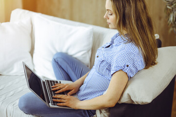 Obraz premium Young woman working on laptop computer sitting indoors during Covid-19 quarantine. Stay at home concept at Coronavirus pandemic
