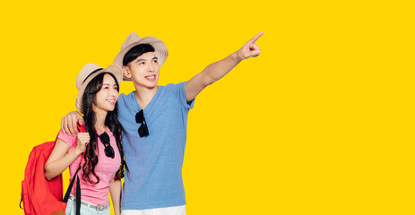 excited Asian couple tourists pointing hand to empty space on isolated yellow banner background