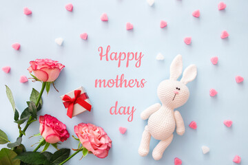Greeting card concept. Bouquet pink roses, amigurumi bunny with letters in word Happy Mothers Day and gift on blue pastel background. Flat lay composition