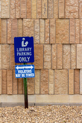 Close up view of a library parking sign in front of an attractive modern limestone wall with unique rough textured vertically aligned natural stone bricks
