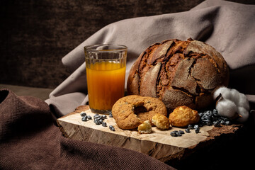 Biscuits, bread and a glass of juice on a wooden stand on a brown background
