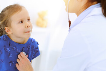 Doctor examining a little girl by stethoscope. Happy smiling child patient at usual medical inspection. Medicine and healthcare concepts