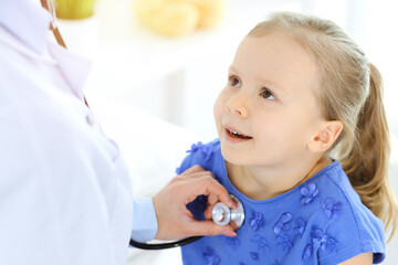 Doctor examining a little girl by stethoscope. Happy smiling child patient at usual medical inspection. Medicine and healthcare concepts