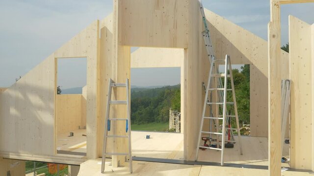CLOSE UP: Aluminum ladders are scattered around the top floor of a CLT house under construction. Contemporary glued-laminated timber house is being built in countryside. Hardwood real estate project.