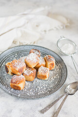 Square curd pancakes, traditional Russian cheesecakes in a gray plate and bowl, with coconut flakes and powdered sugar. Selective focus.