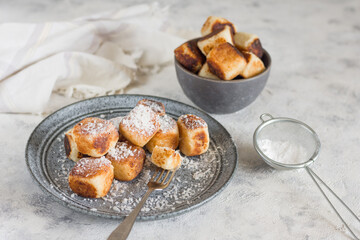 Square curd pancakes, traditional Russian cheesecakes in a gray plate and bowl, with coconut flakes and powdered sugar. Horizontal view.