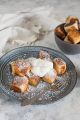 Square curd pancakes, traditional Russian cheese cakes in a gray plate and bowl, with coconut flakes and powdered sugar and sour cream.