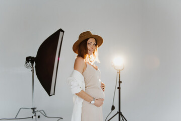 Beautiful young pregnant woman in dress and hat in the studio.