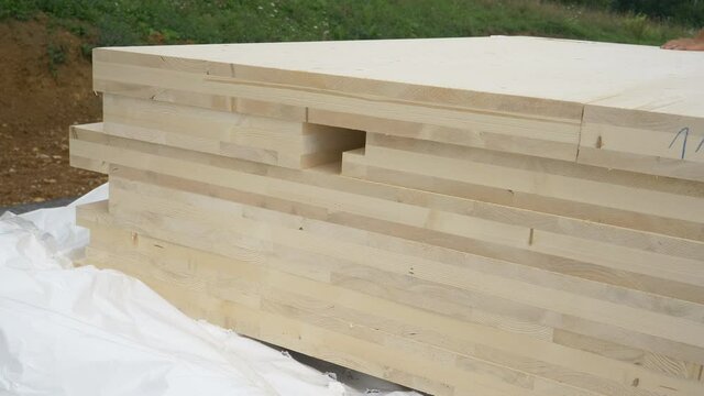 CLOSE UP: A stack of CLT wall panels lie uncovered at a construction site of a modern housing project made of a sustainable materials. Wind blows white tarp off the glued-laminated timber wall boards.