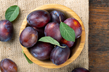 Ripe plums and leaves in a wooden bowl on the table.