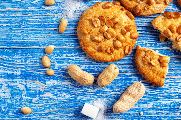 Peanut cookies on a blue wooden background. Sugar and peanuts in a peel are scattered on the table. Selective focus. Space for text.