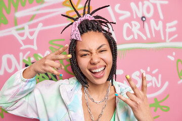 Cool hipster girl makes rap gesture feels crazy and happy smiles broadly has cheeky expression...