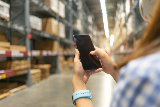 Young Modern Woman Using Touch Screen Mobile Phone In Warehouse Storage.