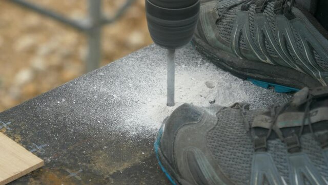 CLOSE UP, DOF: Unrecognizable builder bores a hole in the bitumen covered concrete of a house under construction. Contractor is drilling into the tar covered ground of a new real estate project.