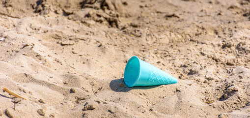 Fototapeta na wymiar a blue plastic ice cream cone in the sand. panorama format