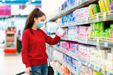 Antiviral protection at public places. A young woman in a medical mask chooses a product in a store. The concept of consumerism and shopping during the coronavirus pandemic