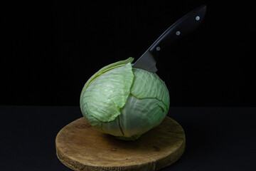 Cabbage on a dark background. A knife stuck in a cabbage on a black background. Young fresh cabbage. Healthy diet