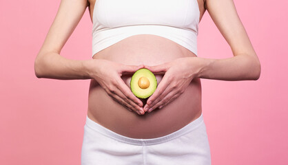 A pregnant girl holds an avocado against her belly.