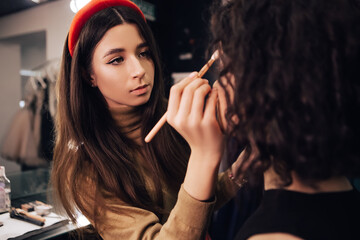 Make up talanted artist doing maquillage to woman applying powder. Visagist using brushes shadows facial professional cosmetics for makeup. Beauty industry studio, image with copy space.
