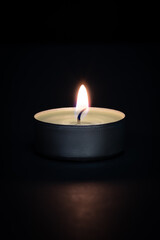 A burning candle on a dark background with a flare in the foreground.