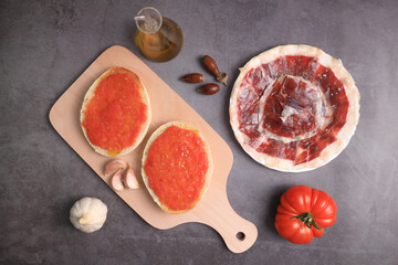 Breakfast of bread toasts with acorn-fed Iberian ham, tomato, garlic and olive oil (tumaca bread) on dark gray background