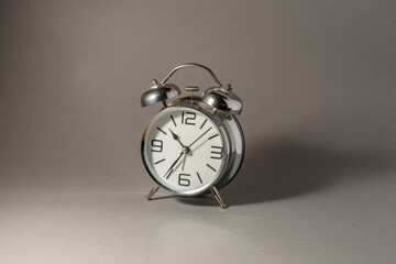 Old silver metal alarm clock on the solid grey background.