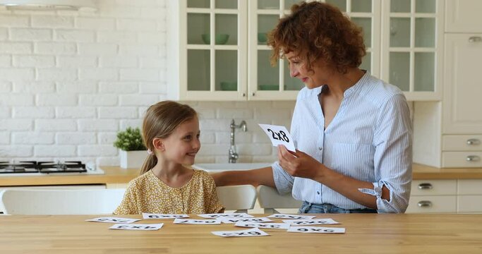 Teacher helps to little girl with mathematics. Mom practice maths with daughter at home, checks knowledge of multiplication in interesting playful way using flashcards. Homeschooling, tutoring concept