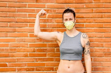 Portrait of a young woman with tattoos wearing a facemask and showing her biceps outdoors