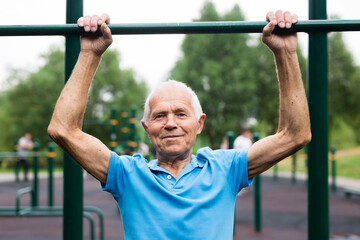 mature cheerful pensioner man doing physical exercises on sports equipped playground