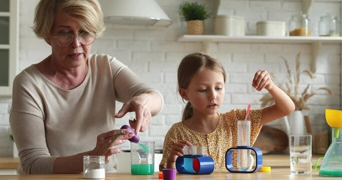 Elderly 60s granny and little grandchild play with science kits at home, enjoy funny interesting introduction to chemistry, learn topics through hands-on experiments. Educational game with kid concept