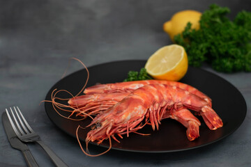 Three 3 grilled giant river prawn on black plate, dark gray stone table.