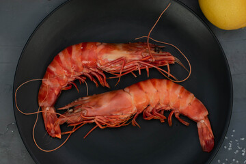 Two 2 grilled giant river prawn on black plate, dark gray stone table.