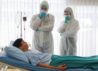 Two thoughtful doctors in white disposable coverall protective suit and mask analyze medical...