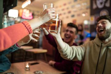 Group of young people hangout in a pub restaurant having fun and toasting, clinking beer glasses....