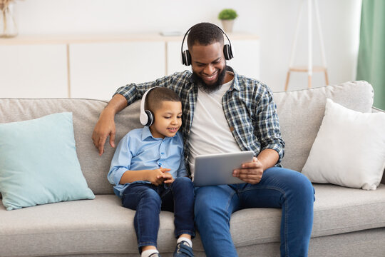 African Father And Kid Wearing Headphones Using Tablet At Home