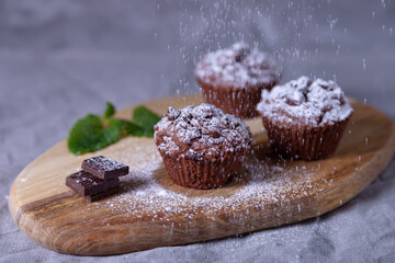 Chocolate muffins on a wooden board, strewed with icing sugar. Homemade baking. Selective focus, close up.
