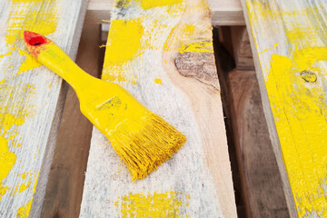 Paint brush painted with yellow color lie on wooden pallet.