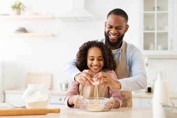 Obraz na płótnie Canvas Happy black man and his child daughter preparing dough